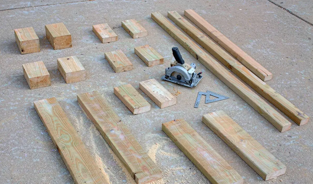 Cut 2x4 and 1x3 pieces laid out on a driveway beside a saw and a speed square