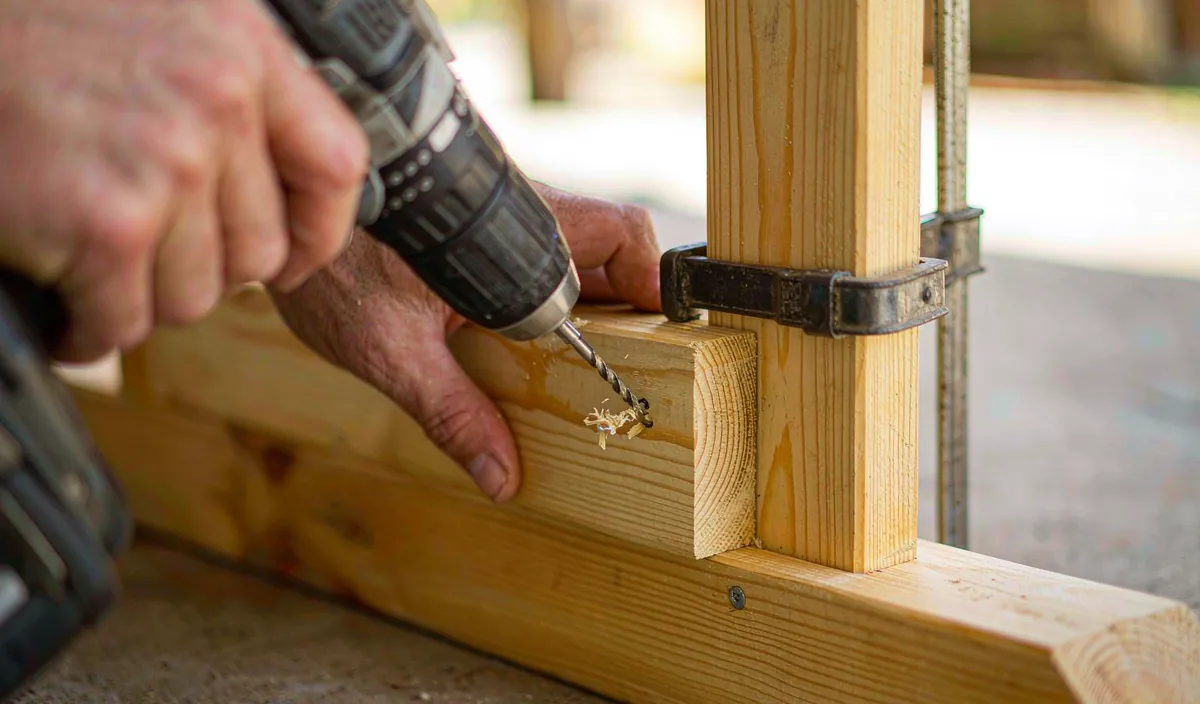 A drill driving a screw through a pre-drilled apron end into a bench leg