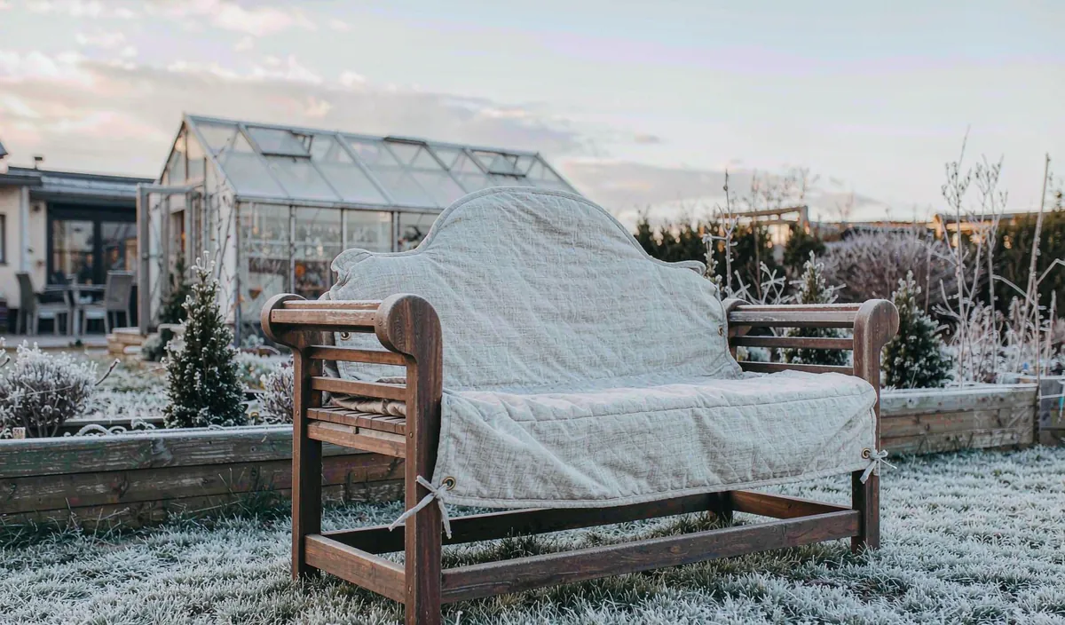 A wooden bench under a breathable cover, tied down, with frost on the grass